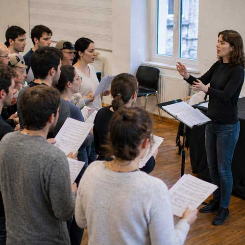 Vue latérale d’une chorale chantant sous la direction d’une cheffe de chœur